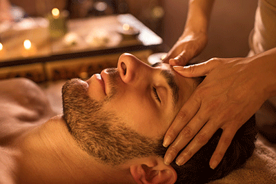 Man getting head massage laying on bed. Head massage oil techniques to calm anxiety and destress.